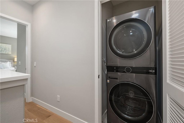 washroom featuring laundry area, stacked washing maching and dryer, baseboards, and wood finished floors