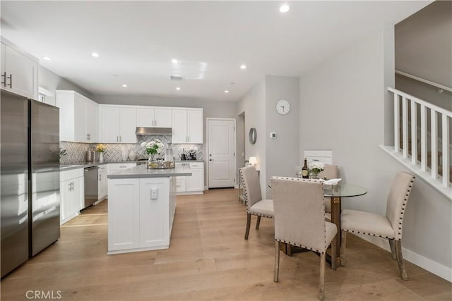 kitchen with a kitchen island, stainless steel appliances, decorative backsplash, under cabinet range hood, and white cabinetry