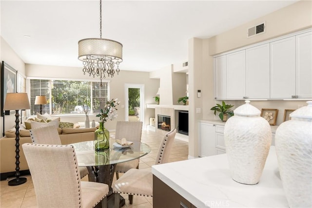 dining space with a glass covered fireplace, a notable chandelier, light tile patterned floors, and visible vents