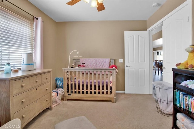 bedroom featuring light carpet, a nursery area, and ceiling fan