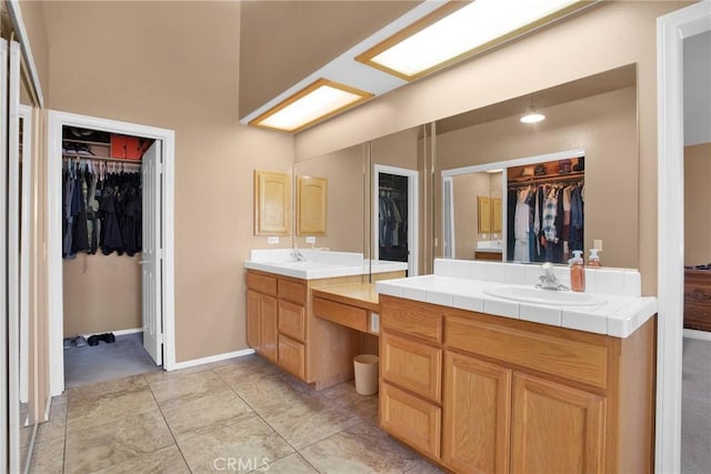 bathroom with a walk in closet, two vanities, baseboards, and a sink