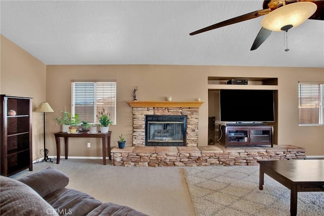 carpeted living area featuring baseboards, a textured ceiling, ceiling fan, and a fireplace