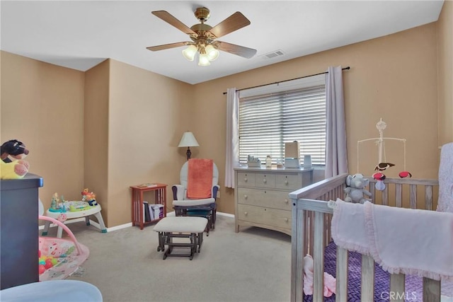 carpeted bedroom with visible vents, a nursery area, a ceiling fan, and baseboards