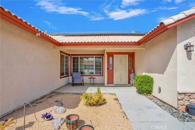 doorway to property featuring solar panels, a tile roof, and stucco siding