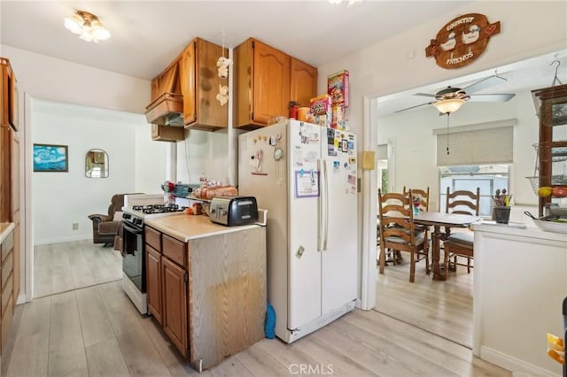 kitchen with light wood-type flooring, range with gas stovetop, brown cabinetry, and freestanding refrigerator