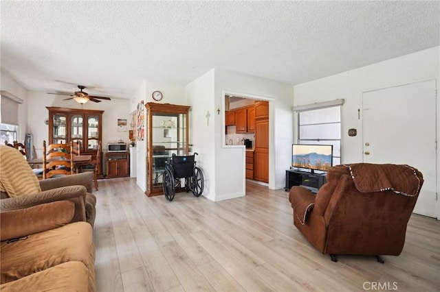 living area featuring a ceiling fan, light wood-type flooring, and a textured ceiling