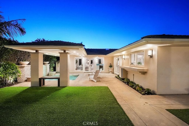 rear view of house with a patio, a yard, an outdoor pool, and stucco siding