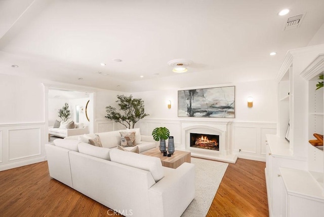 living room with visible vents, recessed lighting, light wood-style flooring, a warm lit fireplace, and a decorative wall