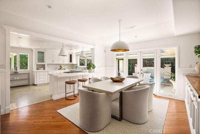 dining room with light wood-style flooring, visible vents, a wainscoted wall, and french doors