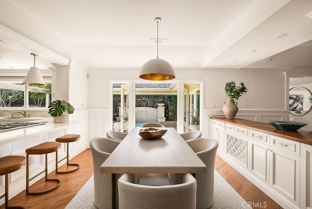 dining space with a decorative wall, visible vents, light wood-type flooring, and wainscoting