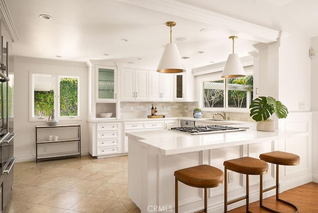 kitchen featuring light countertops, stainless steel gas stovetop, white cabinets, glass insert cabinets, and backsplash