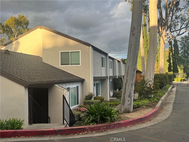 view of side of property with fence, a shingled roof, and stucco siding