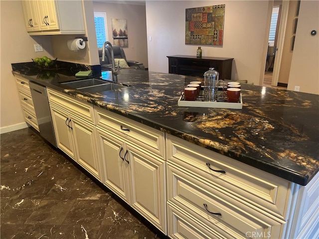 kitchen with a sink, cream cabinets, stainless steel dishwasher, and dark stone countertops
