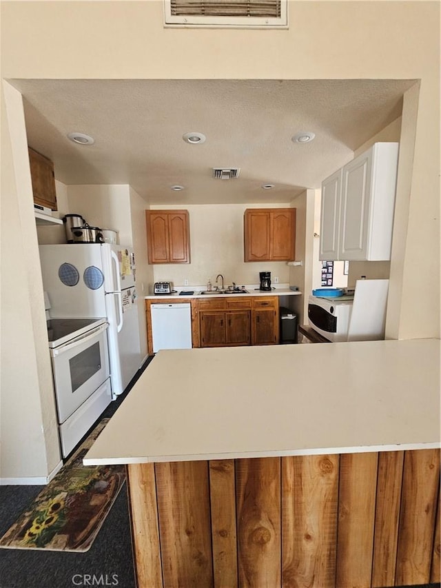 kitchen featuring visible vents, white appliances, light countertops, and a sink