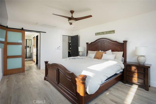bedroom featuring a barn door, a ceiling fan, baseboards, and light wood finished floors