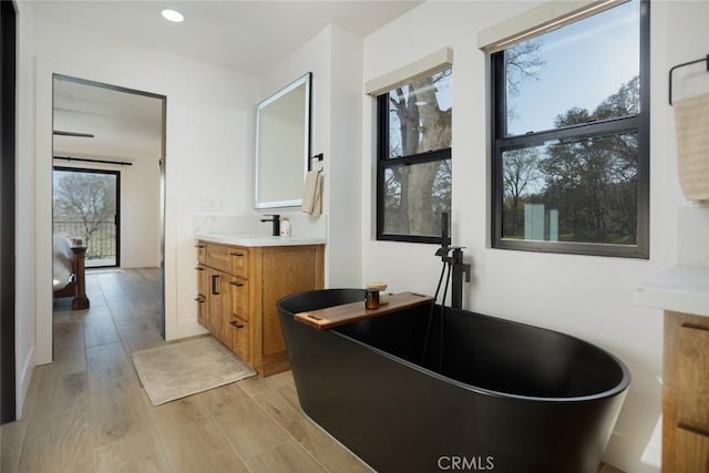 bathroom with vanity, a soaking tub, recessed lighting, and wood finished floors