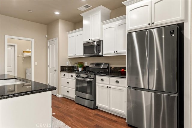 kitchen featuring visible vents, dark stone counters, dark wood-type flooring, white cabinets, and appliances with stainless steel finishes