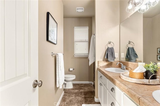 bathroom with double vanity, toilet, baseboards, and a sink