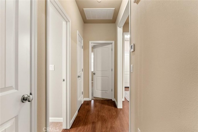 hallway featuring visible vents, baseboards, and dark wood finished floors