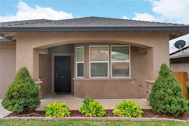 property entrance with a garage, stucco siding, roof with shingles, and fence