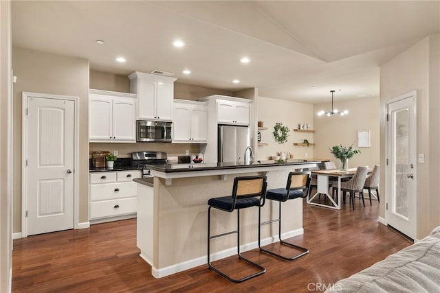 kitchen featuring dark countertops, appliances with stainless steel finishes, a kitchen breakfast bar, white cabinetry, and dark wood-style flooring