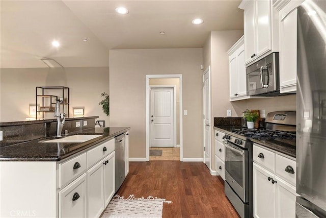 kitchen with dark stone countertops, dark wood finished floors, a sink, appliances with stainless steel finishes, and white cabinetry