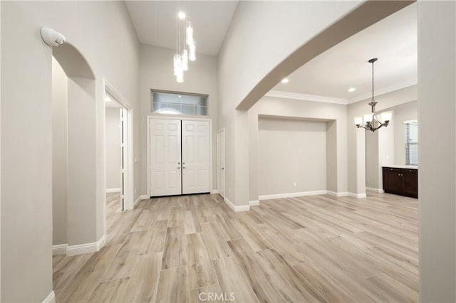 foyer entrance with arched walkways, an inviting chandelier, baseboards, and light wood-style floors