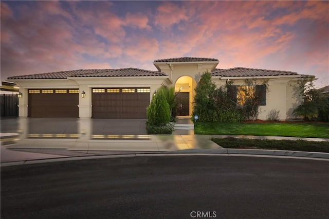 mediterranean / spanish-style house with a garage, stucco siding, driveway, and a tiled roof