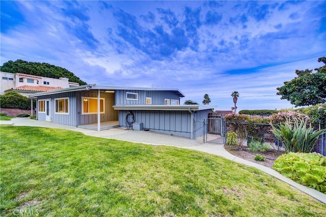 rear view of property featuring a lawn, a gate, a patio, fence, and board and batten siding