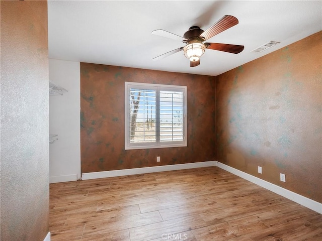 spare room with ceiling fan, visible vents, baseboards, and wood finished floors