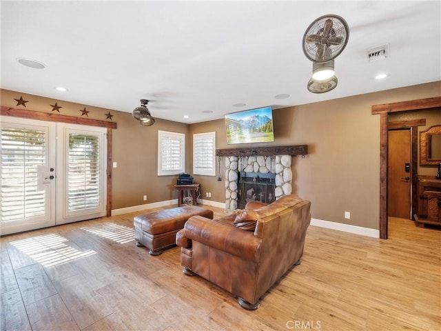 living room featuring visible vents, baseboards, a stone fireplace, french doors, and light wood-type flooring