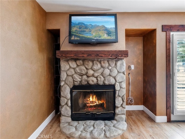 room details with baseboards, a stone fireplace, and wood finished floors