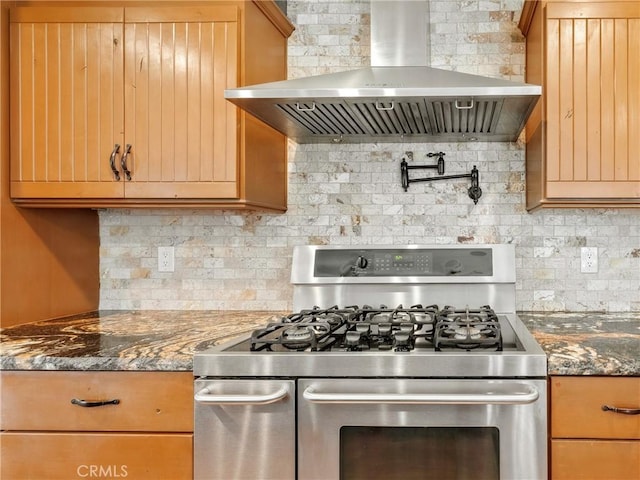 kitchen with decorative backsplash, dark stone counters, wall chimney exhaust hood, and stainless steel range with gas stovetop