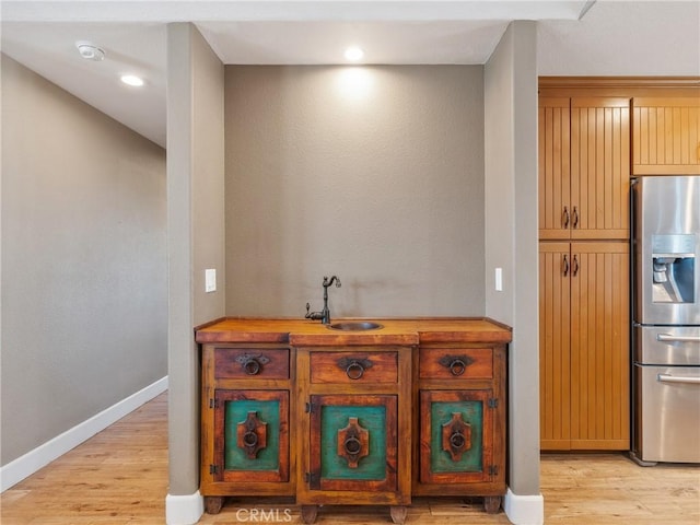 kitchen with a sink, baseboards, stainless steel fridge, and light wood-style floors