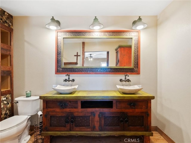 bathroom featuring a sink, baseboards, toilet, and double vanity