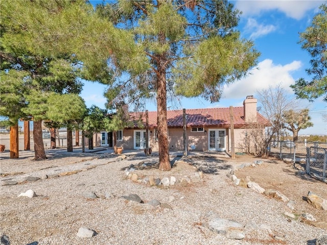 back of property with fence, a tiled roof, stucco siding, french doors, and a chimney