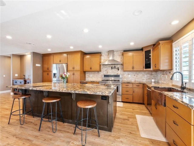 kitchen featuring light wood-type flooring, a large island, tasteful backsplash, stainless steel appliances, and wall chimney range hood