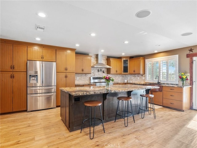 kitchen featuring light wood-type flooring, visible vents, stainless steel fridge with ice dispenser, wall chimney range hood, and stove