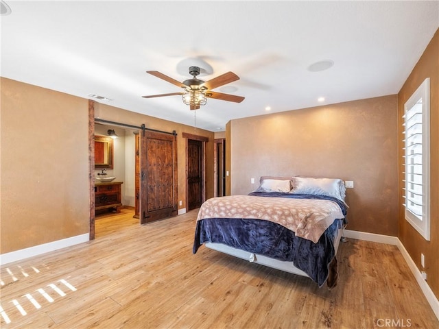 bedroom with visible vents, light wood-style flooring, a barn door, baseboards, and ceiling fan