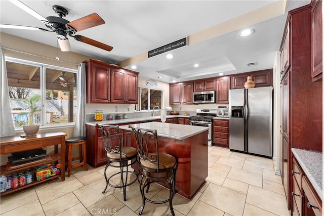 kitchen featuring a kitchen island, recessed lighting, appliances with stainless steel finishes, a raised ceiling, and reddish brown cabinets