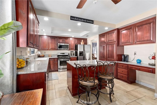 kitchen with a tray ceiling, a sink, stainless steel appliances, dark brown cabinets, and built in desk