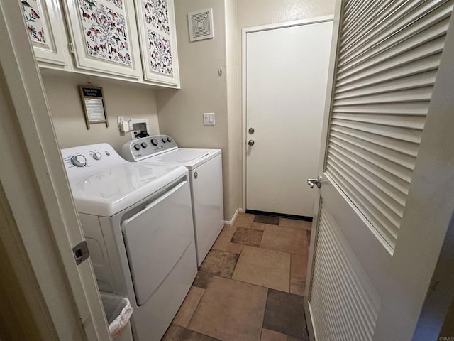 laundry area featuring baseboards, visible vents, cabinet space, stone tile flooring, and washing machine and dryer