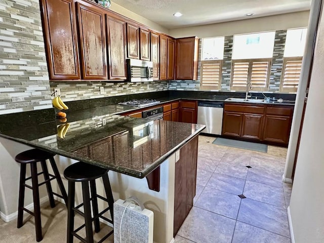 kitchen featuring dark stone countertops, a peninsula, a sink, decorative backsplash, and stainless steel appliances