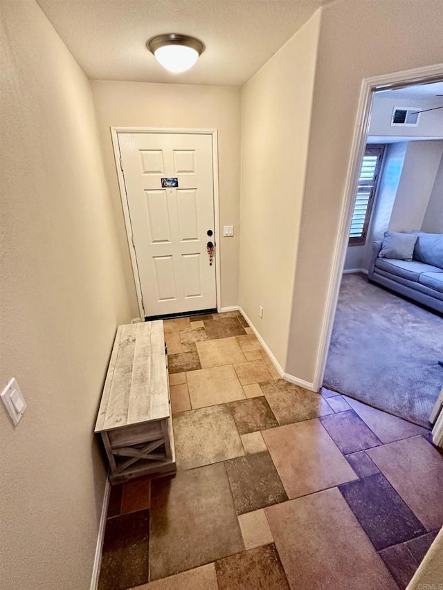 doorway with stone tile flooring, visible vents, and baseboards