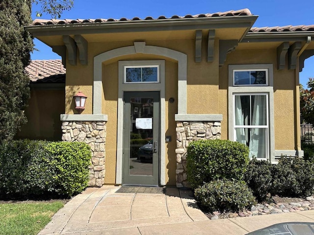 entrance to property featuring a tiled roof, stone siding, and stucco siding