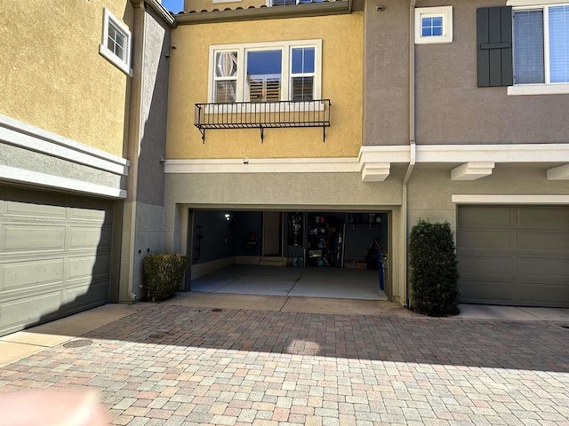 rear view of house featuring a tiled roof, decorative driveway, a garage, and stucco siding