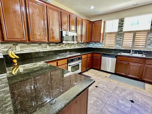 kitchen featuring dark stone countertops, brown cabinetry, a sink, appliances with stainless steel finishes, and tasteful backsplash