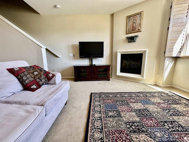 carpeted living room featuring a glass covered fireplace, stairway, and baseboards