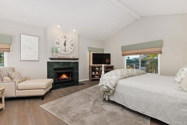 bedroom with a high end fireplace, lofted ceiling with beams, and wood finished floors