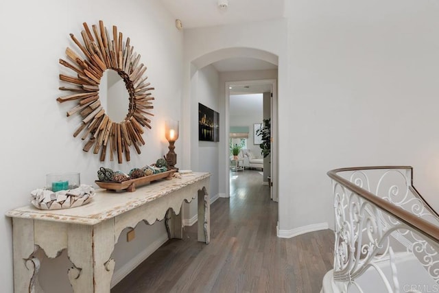 hall with dark wood finished floors, arched walkways, and baseboards